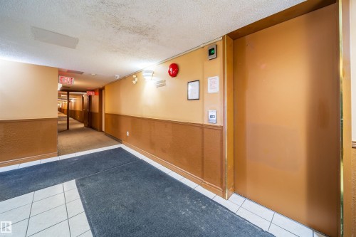 Building corridor featuring tile flooring, wainscoting, and an elevator with a metallic door - 213 5065 31 Avenue, Edmonton, AB - Indoor Photo Showing Other Room