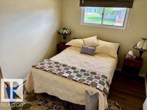 Room featuring a double-hung window with a fabric roller shade, cream-painted walls, and wood-finish flooring - 4805 53Ave, Willingdon, AB - Indoor Photo Showing Bedroom