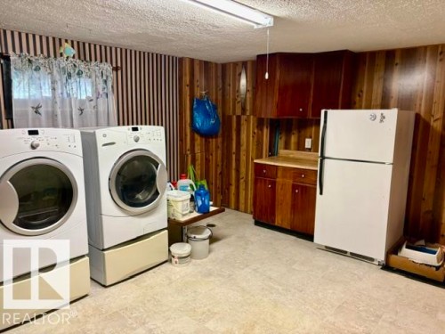 Practical utility space featuring wood-finish wall paneling, a built-in wood-finish cabinet with a light-tone countertop, and light-tone flooring - 4805 53Ave, Willingdon, AB - Indoor Photo Showing Laundry Room
