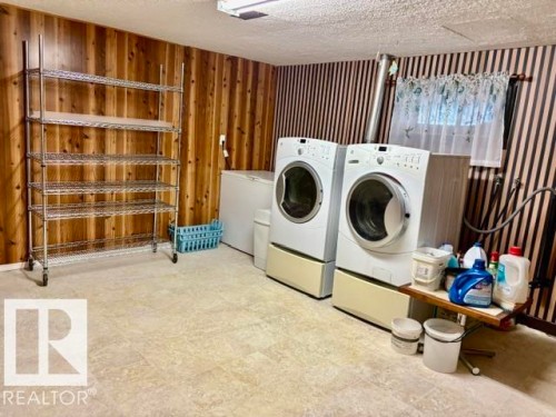 Laundry area featuring light-toned tile flooring, wood paneling, and a window with a sheer curtain - 4805 53Ave, Willingdon, AB - Indoor Photo Showing Laundry Room