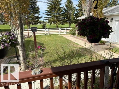 Expansive green lawn with a white picket fence, mature evergreen trees, a concrete pathway, and a detached garage featuring a white door - 4805 53Ave, Willingdon, AB - Outdoor