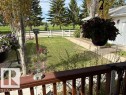 Expansive green lawn with a white picket fence, mature evergreen trees, a concrete pathway, and a detached garage featuring a white door - 4805 53Ave, Willingdon, AB  - Outdoor 