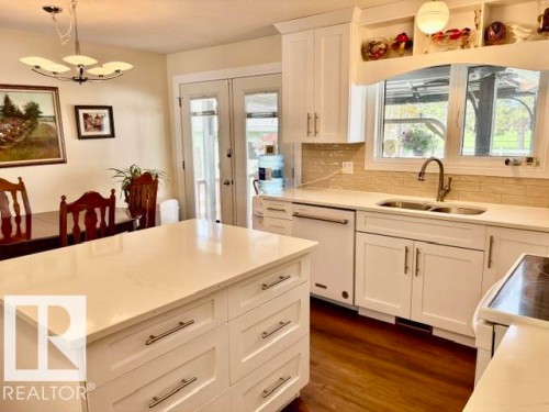Kitchen featuring a central island with a light-toned countertop, white cabinetry with silver-tone hardware, wood-finish flooring, and a double-basin sink with a gooseneck faucet - 4805 53Ave, Willingdon, AB - Indoor