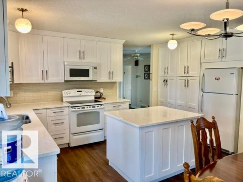 Kitchen featuring white cabinetry, light-toned countertops, a central island, wood-finish flooring, and subway tile backsplash - 4805 53Ave, Willingdon, AB - Indoor Photo Showing Kitchen