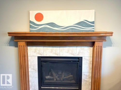 Fireplace featuring a wood-finished mantel and surround with fluted pilasters, tile facing, and a built-in firebox with a metal screen - 1206 Mckinney Court, Edmonton, AB - Indoor Photo Showing Living Room With Fireplace