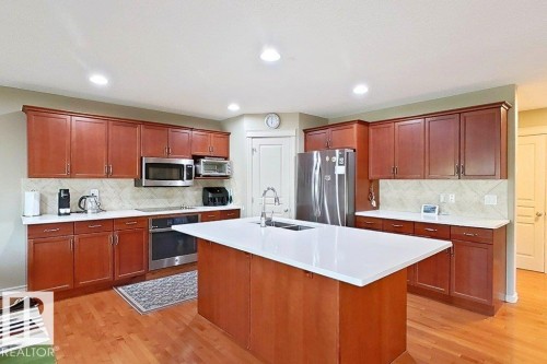 Kitchen featuring wood-finish flooring, recessed lighting, and a central island with a solid surface countertop and undermount sink - 1206 Mckinney Court, Edmonton, AB - Indoor Photo Showing Kitchen With Double Sink