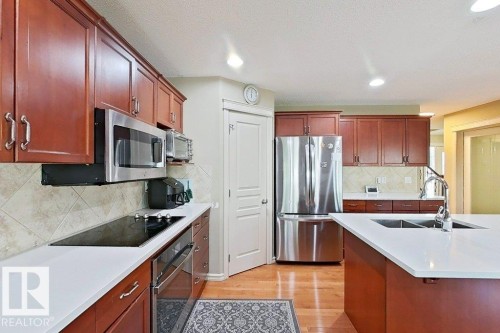 Kitchen featuring cherry wood cabinetry, stainless steel appliances, light-toned tile backsplash, light-toned countertops, and wood-finish flooring - 1206 Mckinney Court, Edmonton, AB - Indoor Photo Showing Kitchen With Double Sink With Upgraded Kitchen