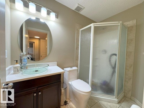 Bathroom featuring a quadrant shower enclosure, dark wood-finish vanity with a glass vessel sink, white countertop, and a circular mirror - 1206 Mckinney Court, Edmonton, AB - Indoor Photo Showing Bathroom