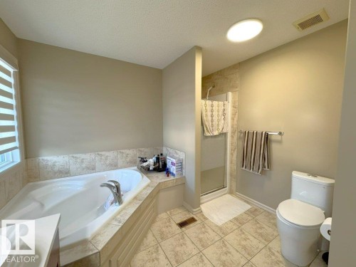 Full bathroom featuring a built-in soaking tub, a stand-up shower with tiled surround, a toilet, a sun tunnel, and neutral-toned floor tile - 1206 Mckinney Court, Edmonton, AB - Indoor Photo Showing Bathroom