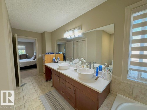 Bathroom vanity with dual vessel sinks, white countertop, and wood-finish cabinetry - 1206 Mckinney Court, Edmonton, AB - Indoor Photo Showing Bathroom