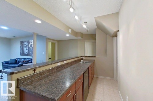 Lower level entertainment area featuring a wet bar with integrated sink, wood-finish cabinetry, and a stone-look countertop - 1206 Mckinney Court, Edmonton, AB - Indoor