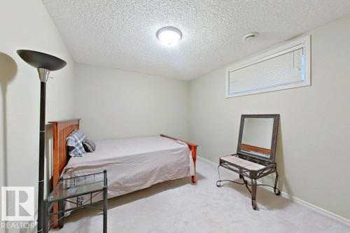 Light beige carpeting and neutral wall tones define this room, featuring a rectangular window with blinds, a white ceiling, and a flush-mount ceiling light fixture - 1206 Mckinney Court, Edmonton, AB - Indoor Photo Showing Bedroom