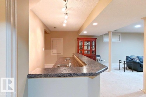 Built-in wet bar with a dark speckled countertop and stainless steel sink - 1206 Mckinney Court, Edmonton, AB - Indoor