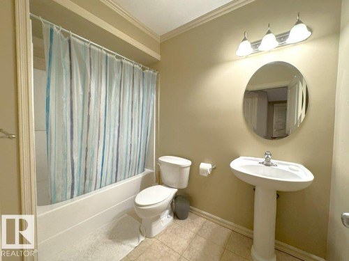 Full bathroom featuring a white pedestal sink, circular mirror, and a three-light vanity fixture - 1206 Mckinney Court, Edmonton, AB - Indoor Photo Showing Bathroom