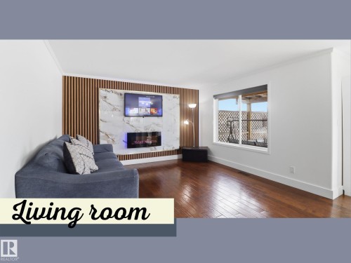 Living room featuring hardwood floors, a prominent decorative wall panel with a fireplace, and a large window - 3243 26 Street, Edmonton, AB - Indoor With Fireplace