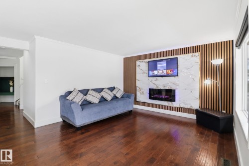 The living area features polished hardwood floors, a decorative accent wall with vertical wood paneling and a marble-patterned inset, and an integrated fireplace - 3243 26 Street, Edmonton, AB - Indoor Photo Showing Living Room With Fireplace