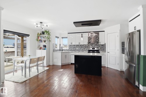 The kitchen and dining area feature hardwood flooring, white cabinetry with a patterned backsplash, and a central island with a dark finish - 3243 26 Street, Edmonton, AB - Indoor Photo Showing Kitchen With Upgraded Kitchen