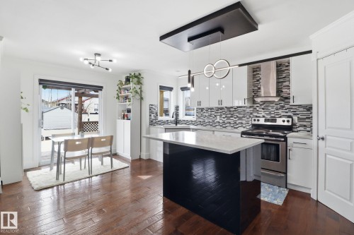 The open concept kitchen and dining area features hardwood floors, a kitchen island with a light-colored countertop, stainless steel appliances, and a tiled backsplash - 3243 26 Street, Edmonton, AB - Indoor Photo Showing Kitchen With Upgraded Kitchen
