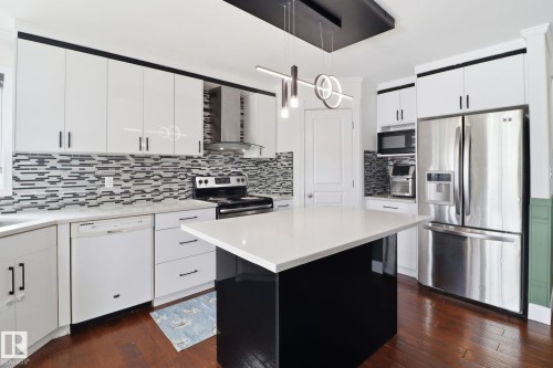 The kitchen features white cabinetry with contrasting trim, a white island with a countertop, stainless steel appliances, and a tiled backsplash - 3243 26 Street, Edmonton, AB - Indoor Photo Showing Kitchen With Upgraded Kitchen