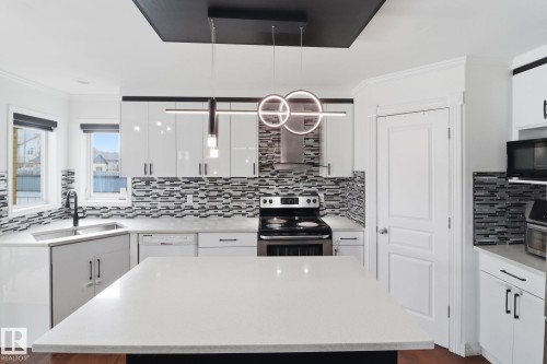 Contemporary kitchen featuring white cabinetry, a large center island with a light-colored countertop, and a patterned tile backsplash - 3243 26 Street, Edmonton, AB - Indoor Photo Showing Kitchen With Upgraded Kitchen
