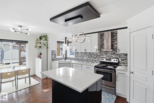 The kitchen features a central island with a light-colored countertop, white cabinetry, a stainless steel range, and a patterned tile backsplash - 3243 26 Street, Edmonton, AB - Indoor Photo Showing Kitchen With Upgraded Kitchen