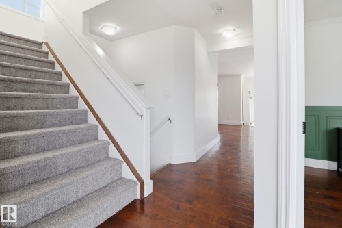 Entryway featuring a carpeted staircase with a wood handrail, hardwood flooring, and white walls with a green accent wall - 3243 26 Street, Edmonton, AB - Indoor Photo Showing Other Room