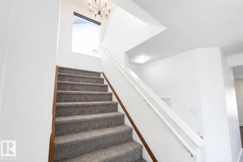 Inviting staircase with carpeted treads and a prominent window providing natural light - 3243 26 Street, Edmonton, AB - Indoor Photo Showing Other Room