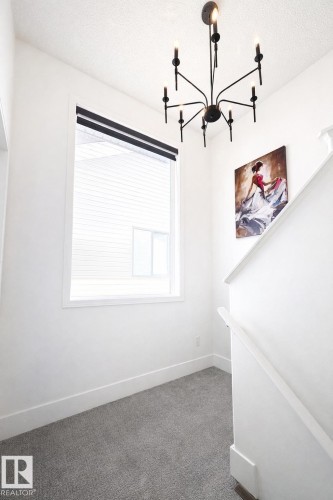 The property features a contemporary black chandelier, a window with blinds, and gray carpeted flooring - 3243 26 Street, Edmonton, AB - Indoor Photo Showing Other Room