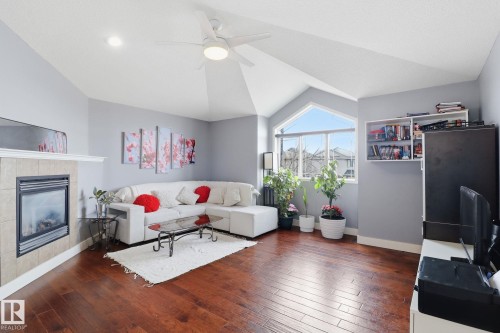 Living area featuring hardwood floors, a tiled fireplace, and a large window providing natural light - 3243 26 Street, Edmonton, AB - Indoor Photo Showing Living Room With Fireplace