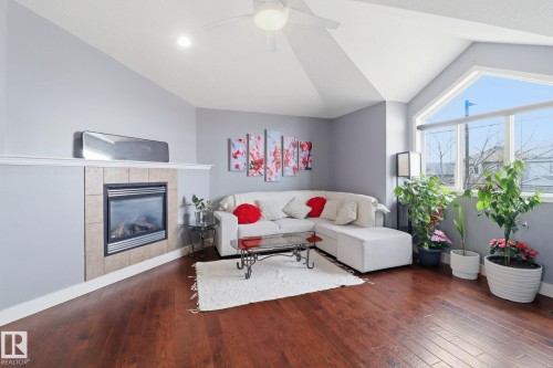 Living room featuring rich hardwood floors, a tiled fireplace with a mantel, and a large window providing natural light - 3243 26 Street, Edmonton, AB - Indoor Photo Showing Living Room With Fireplace