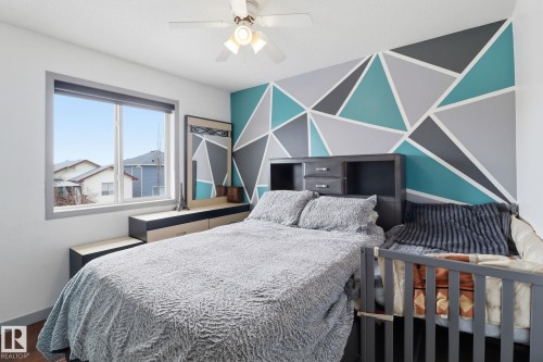 This room features a window providing natural light, a ceiling fan, and a decorative accent wall with geometric patterns - 3243 26 Street, Edmonton, AB - Indoor Photo Showing Bedroom