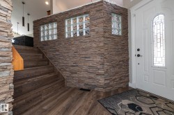 Entryway featuring a white paneled door with leaded glass, stone accent wall with glass block windows, wood-finish flooring, and a staircase with a wooden handrail - 