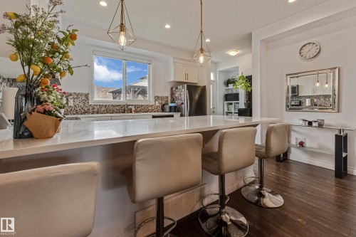 Kitchen island featuring a substantial countertop, pendant lighting, white cabinetry, and stainless steel appliances - 8131 Chappelle Way, Edmonton, AB - Indoor