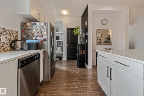 Kitchen featuring white cabinetry, stainless steel dishwasher, mosaic tile backsplash, wood-finish flooring, and a stone countertop - 8131 Chappelle Way, Edmonton, AB - Indoor Photo Showing Kitchen