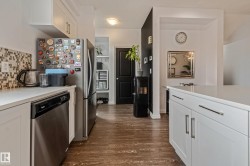Kitchen featuring white cabinetry, stainless steel dishwasher, mosaic tile backsplash, wood-finish flooring, and a stone countertop - 