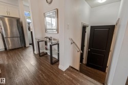 Wood-finish flooring throughout, complemented by a stainless steel refrigerator and white cabinetry - 