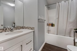 Bathroom featuring a white vanity with an undermount sink, mosaic tile backsplash, and a shower/tub combination with a white surround - 
