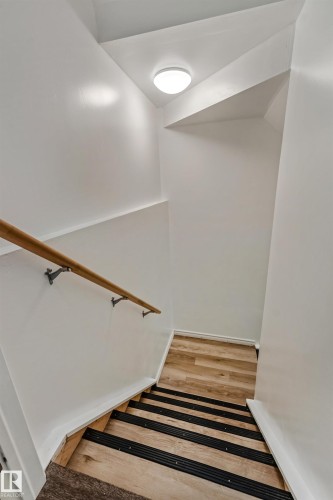 Staircase featuring wood-finish treads with black anti-slip strips, a light wood handrail with metal brackets, white painted walls, and an overhead flush-mount light fixture - 8131 Chappelle Way, Edmonton, AB - Indoor Photo Showing Other Room
