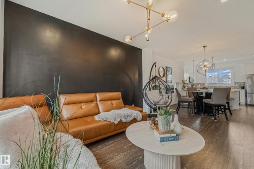 Open-concept living area featuring wood-finish flooring, a contemporary chandelier, and a dark accent wall - 8131 Chappelle Way, Edmonton, AB - Indoor