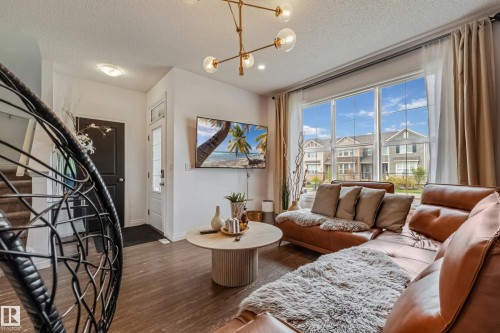 Living area with wood-finish flooring, large window with neighborhood views, and a contemporary chandelier - 8131 Chappelle Way, Edmonton, AB - Indoor Photo Showing Living Room