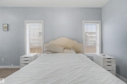 Light-filled room featuring two windows with horizontal blinds, an upholstered headboard with nailhead trim, and coordinating white multi-drawer storage units - 
