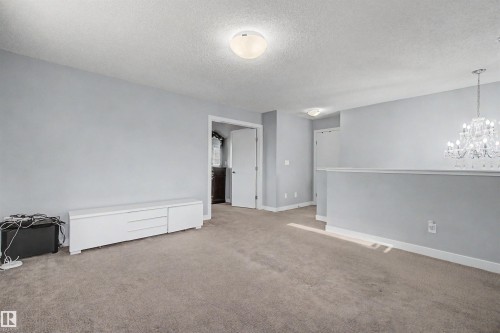Carpeted room with light gray walls, white trim, and a clear crystal chandelier - 1602 Chapman Way, Edmonton, AB - Indoor Photo Showing Other Room