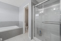 Bathroom featuring a glass-enclosed shower with frosted accents, a built-in tub with tile surround, and light gray wall tiling - 