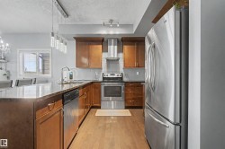 Kitchen featuring wood cabinetry, stainless steel appliances, dark stone countertops, a tile backsplash, and wood-finish flooring - 
