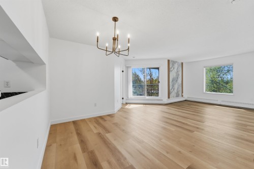 Open-concept living space with wood-finish flooring, a contemporary chandelier, large windows, and a dedicated accent wall featuring vertical stone-look paneling - 302 2508 50 Street Nw, Edmonton, AB - Indoor