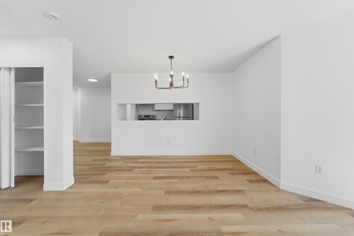 Spacious living area featuring wood-finish flooring, a modern chandelier, and a pass-through window to the kitchen - 302 2508 50 Street Nw, Edmonton, AB - Indoor Photo Showing Other Room