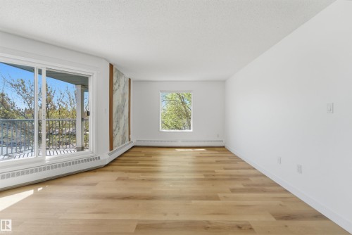 Spacious room featuring wood-finish flooring, a large sliding glass door opening to an outdoor balcony, an accent wall with a vertical panel design, and crisp white walls - 302 2508 50 Street Nw, Edmonton, AB - Indoor Photo Showing Other Room