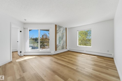 Spacious room featuring wood-finish flooring, white walls, and baseboard heating - 302 2508 50 Street Nw, Edmonton, AB - Indoor