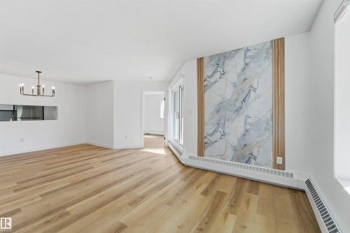 Bright open-concept living area featuring light wood-finish flooring, a contemporary accent wall with a marble-effect panel and vertical wood slat details, a built-in wall cutout, and a modern black chandelier - 302 2508 50 Street Nw, Edmonton, AB - Indoor Photo Showing Other Room