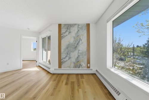 Spacious interior featuring wood-finish flooring, a contemporary accent wall with a marble-effect panel and vertical wood slats, and a large picture window - 302 2508 50 Street Nw, Edmonton, AB - Indoor Photo Showing Other Room